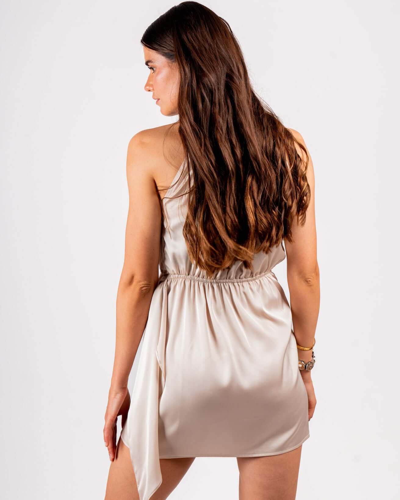 woman wearing a sleeveless, satin mini dress in a soft champagne color. The dress has a high halter neckline and a relaxed, draped fit, creating an elegant and chic look.