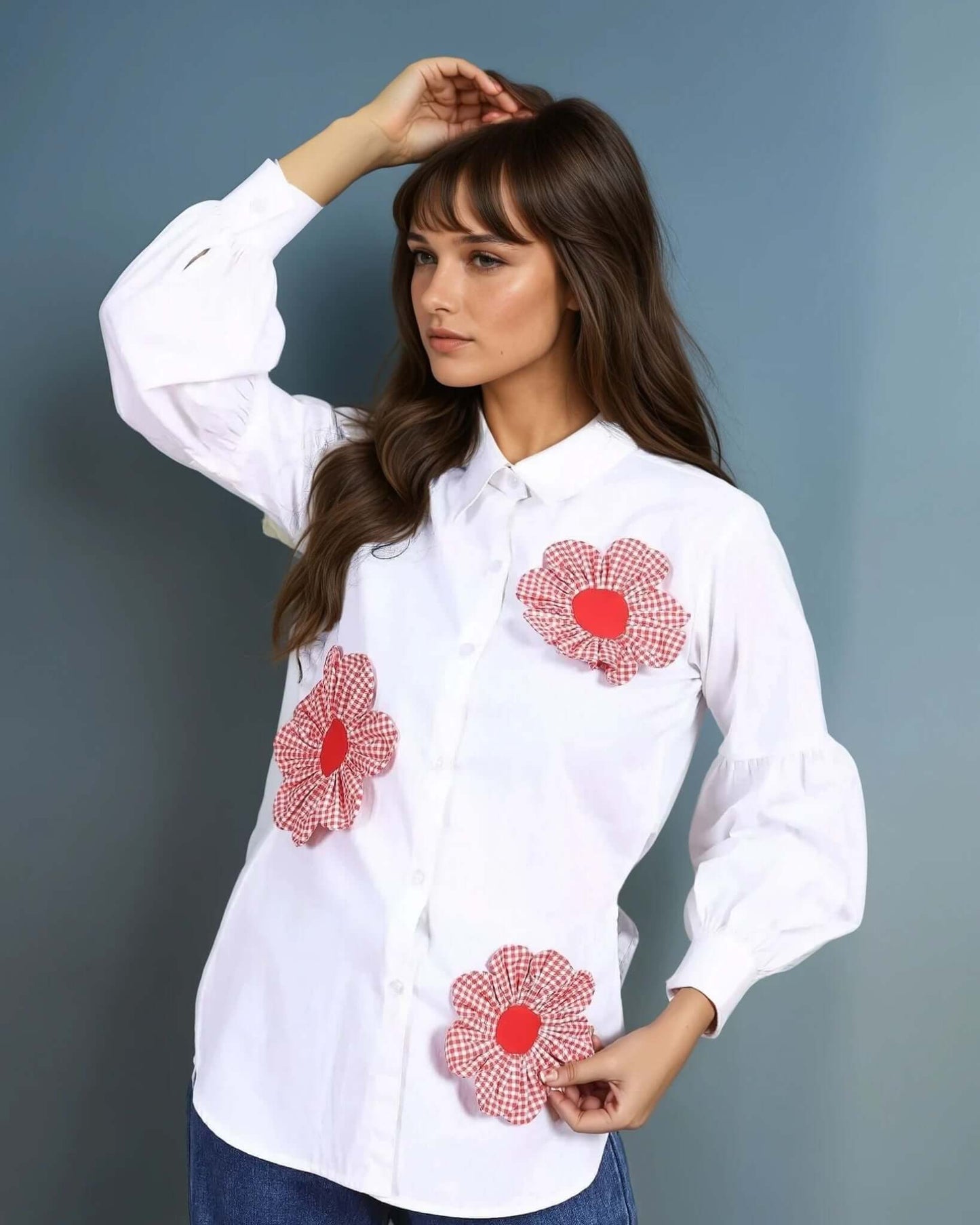 A model wearing a white oversized button-down shirt adorned with red gingham floral appliquΓ©s, paired with high-waisted wide-leg denim jeans and white loafers. The outfit blends casual elegance with a touch of statement detailing, perfect for chic everyday wear.