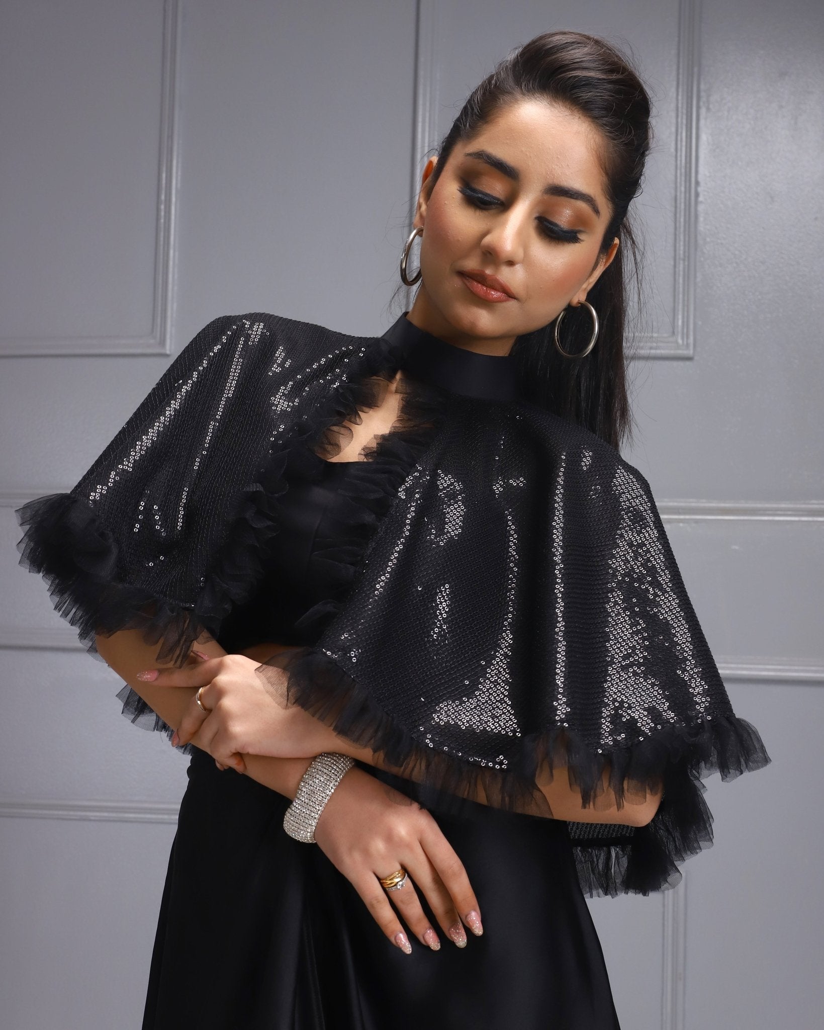 A woman in a glamorous black outfit from House Of Majisha, with a sequined cape and a flowing skirt, posed with flair.