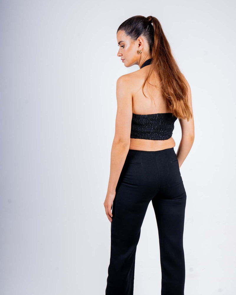 Woman wearing a stylish black halter top with fringe details and a backless design, paired with black pants, perfect for evening wear.