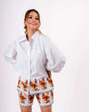 Woman smiling while wearing a white floral coord set with a loose shirt and relaxed shorts crafted from soft twill cotton.