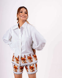 Woman smiling while wearing a white floral coord set with a loose shirt and relaxed shorts crafted from soft twill cotton.