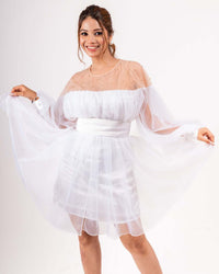 Woman wearing a white organza balloon dress with a delicate net overlay, satin slip, and voluminous sleeves, smiling and posing elegantly.