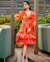 A model showcasing the Starlit Elegance Coord Dress by House Of Majisha, featuring a vibrant orange floral print with a flattering V-neck and full sleeves, perfect for brunch outings or picnics. The dress is knee-length with playful ruffles and a stylish cutout at the waist, embodying a chic skater style.