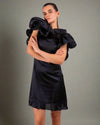 Woman wearing a ruffled black dress from House Of Majisha, crossing her arms and posing confidently against a neutral background.