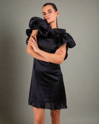 Woman wearing a ruffled black dress from House Of Majisha, crossing her arms and posing confidently against a neutral background.