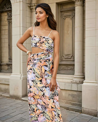 Model wearing a tropical print co-ord set featuring a ruched crop top with thin straps and a draped asymmetrical skirt from House Of Majisha. The outfit showcases vibrant leaf patterns in shades of orange, purple, and green, perfect for a stylish summer or resort look.