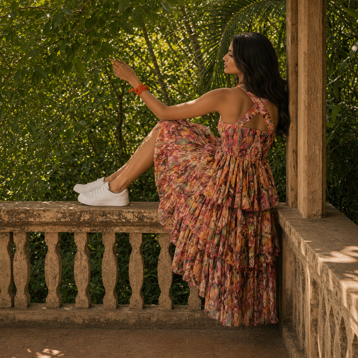 Woman in a floral dress from house of majisha sitting on a stone ledge with greenery in the background.