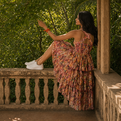 Woman in a floral dress from house of majisha sitting on a stone ledge with greenery in the background.