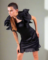 Woman in a House Of Majisha black satin dress with dramatic ruffle detailing, standing with a composed and elegant stance.