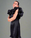 A woman in a House Of Majisha black dress with dramatic ruffled sleeves, standing with a poised and confident expression.