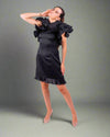 A woman wearing a House Of Majisha black dress with statement ruffles, posing confidently with her arms crossed.