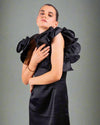 Woman in a black dress from House Of Majisha, showcasing large ruffled shoulders and a chic satin finish.