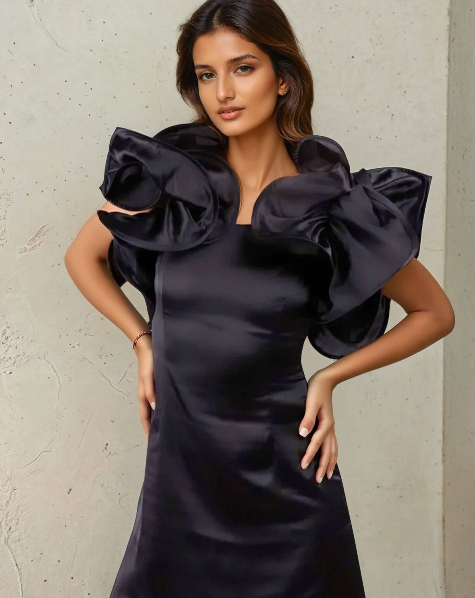 A woman in a House Of Majisha black dress with oversized ruffles, striking a strong pose with arms crossed.