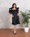 Elegant woman in a black satin dress with dramatic ruffled sleeves and a flared hemline.