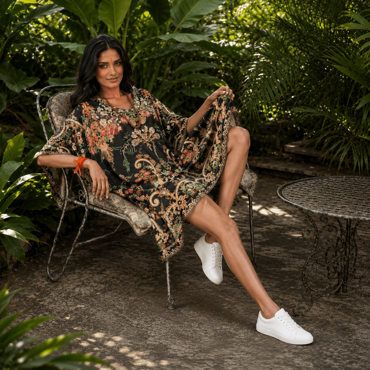 Woman in a house of majisha floral kaftan dress sitting on a chair in a garden setting.