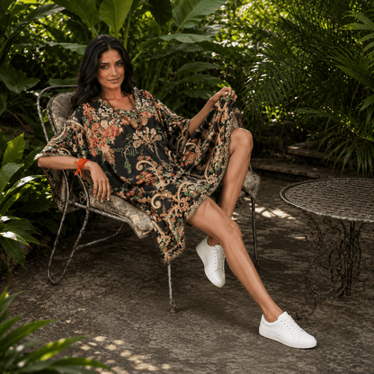 Woman in a house of majisha floral kaftan dress sitting on a chair in a garden setting.