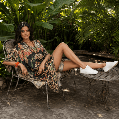 Woman in a house of majisha floral kaftan dress sitting on a chair in a garden setting.