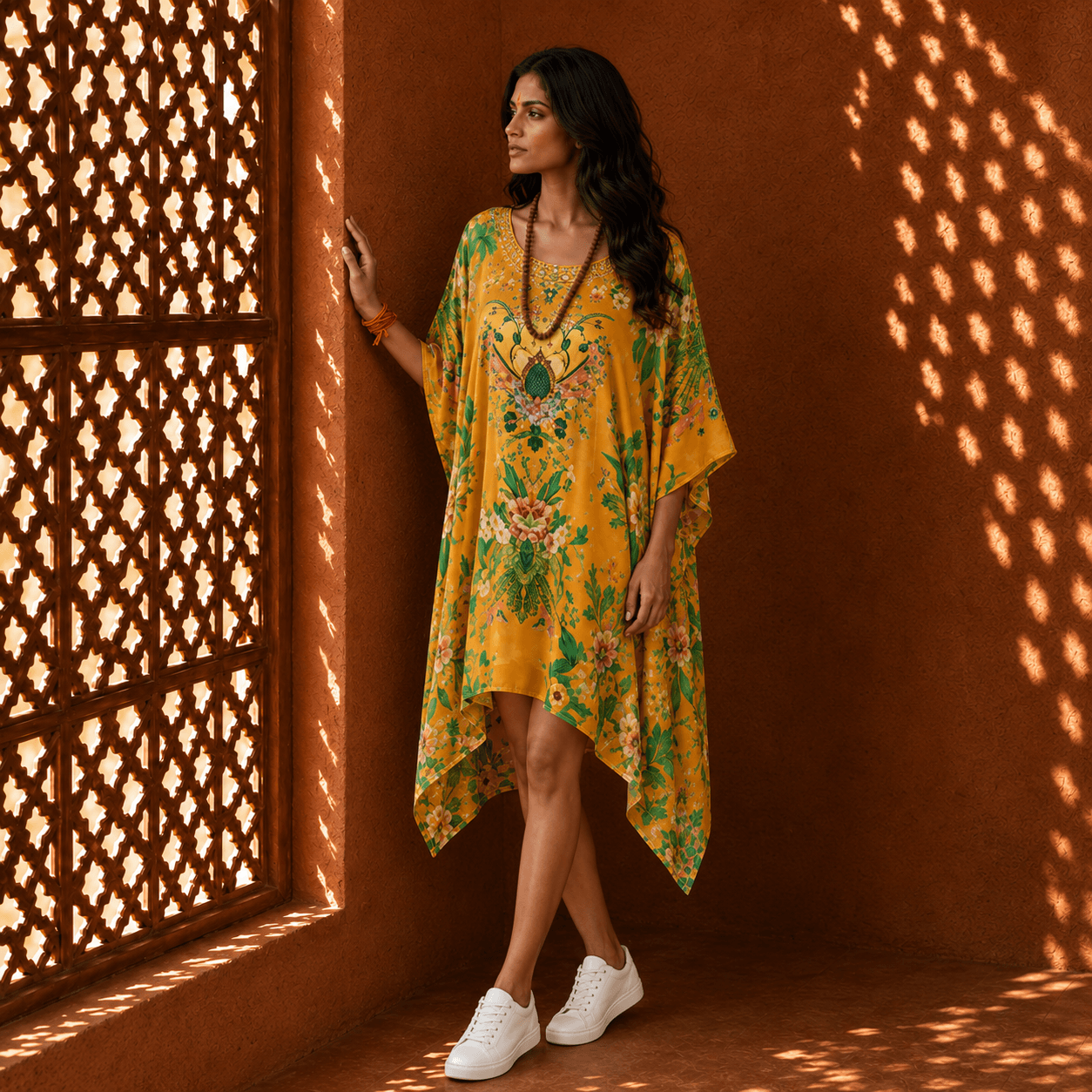 Woman in a house of majisha yellow floral dress standing against a textured wall with lattice shadows.