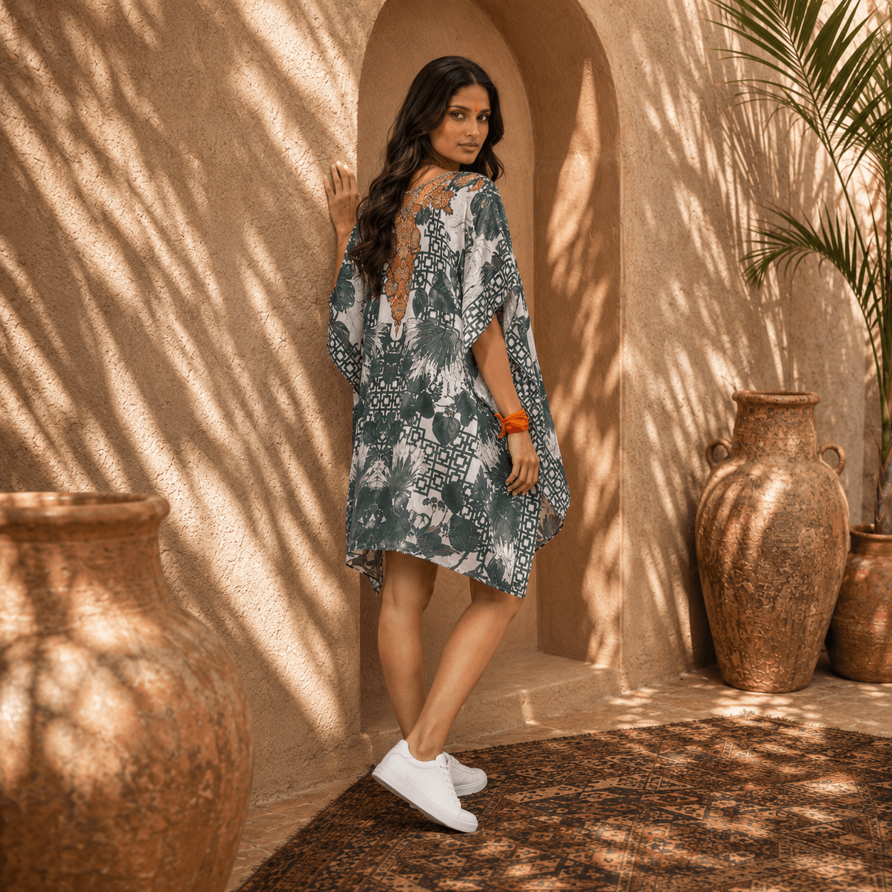 Woman in a house of majisha patterned kaftan dress standing in front of a textured wall with large pots.