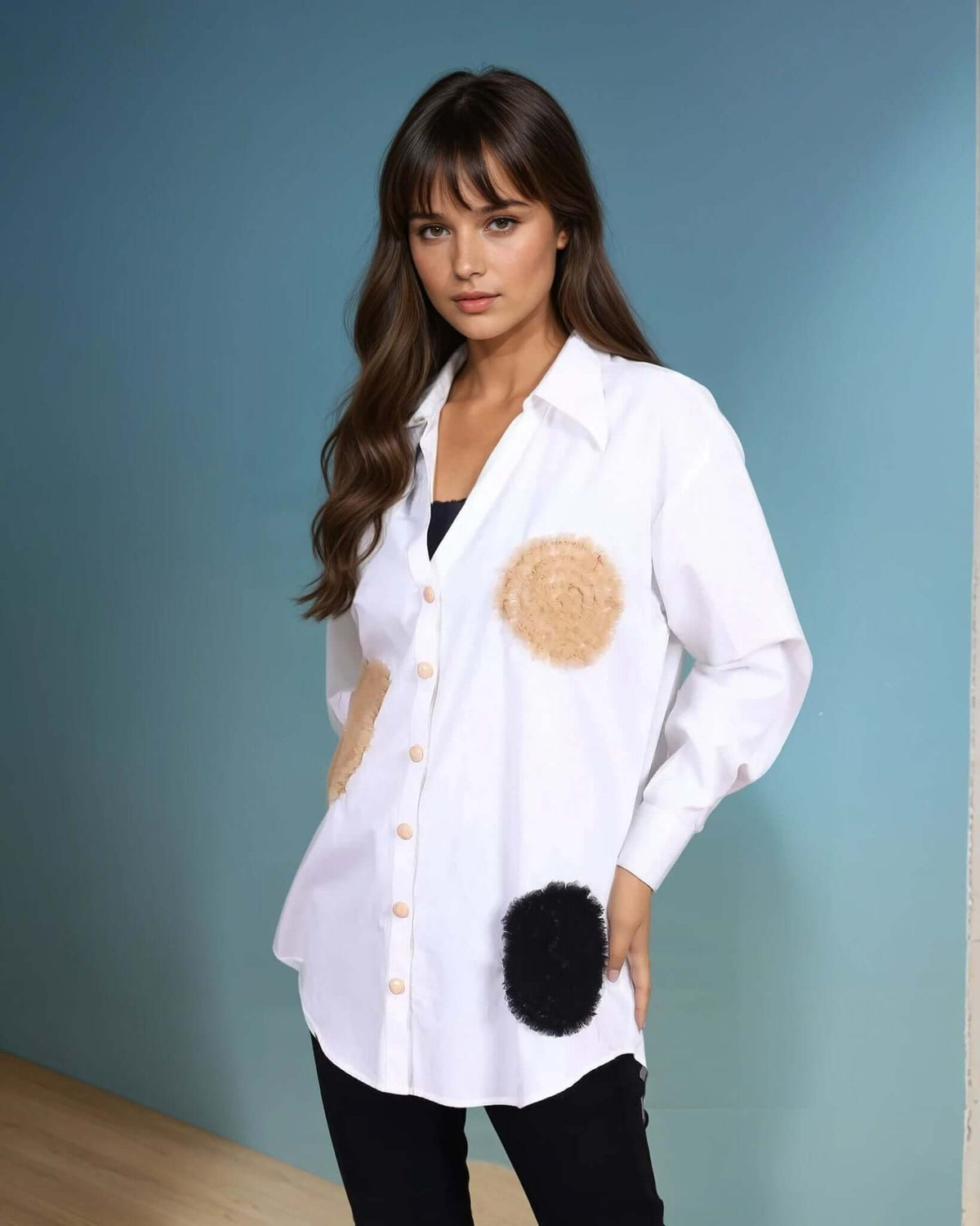 A model in a white oversized button-down shirt with artistic beige and black circular fabric appliqués. The shirt features a relaxed fit, light brown buttons rom House Of Majisha, and is paired with slim black pants and pointed-toe heels, creating a modern and chic monochrome look