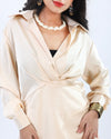 A poised woman in a cream satin wrap dress stands gracefully