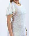 Elegant woman in a short, glittering sequin dress with sheer sleeves and high heels, embodying sophistication and style